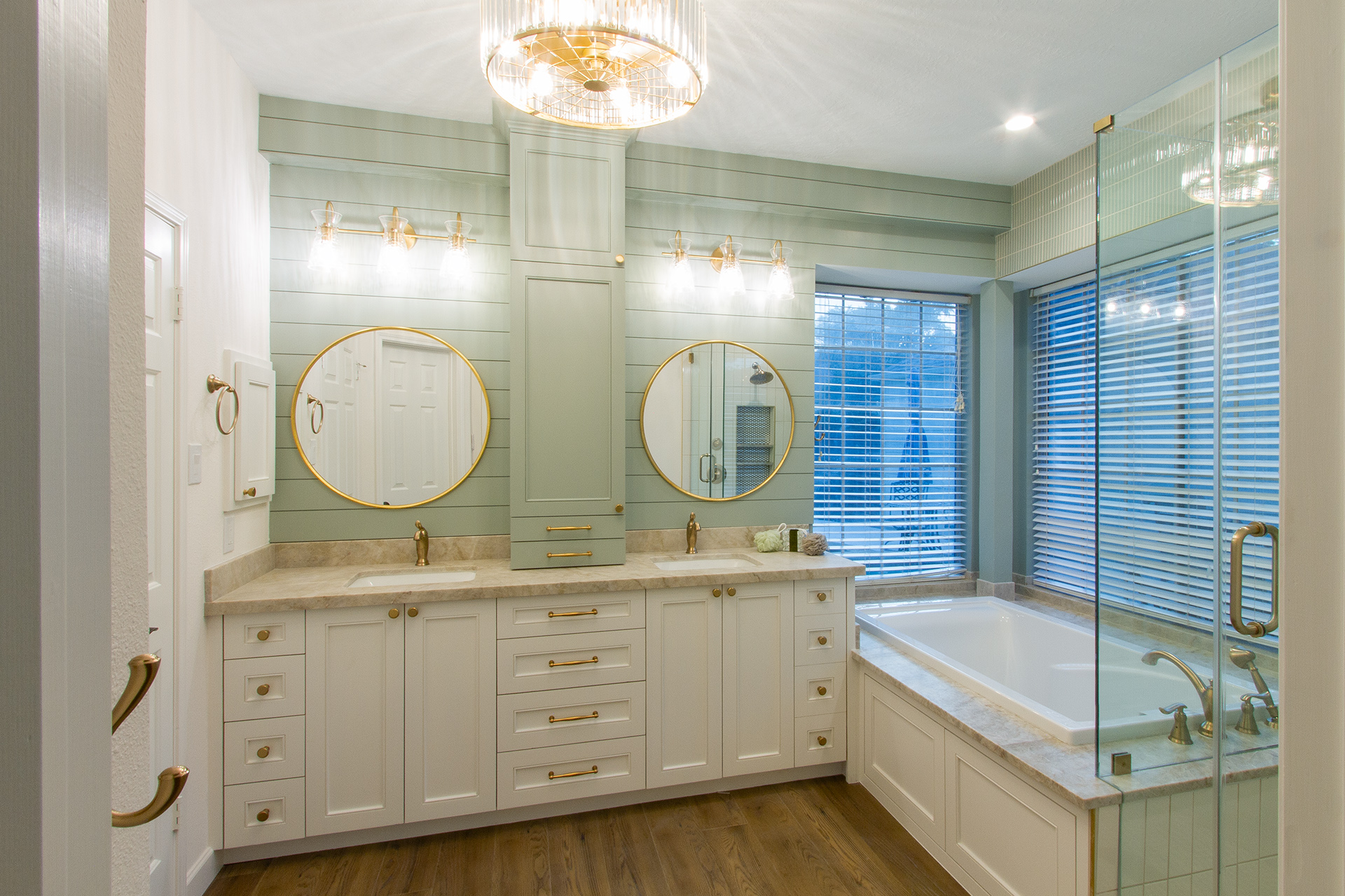 Bathroom with twin round mirrors above a cream double vanity, a drop-in tub and a glass shower enclosure