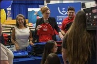 Families queuing at a table of blue and red branded backpacks in a school cafeteria