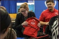 A volunteer in a red shirt handing a red backpack to a woman at the giveaway table