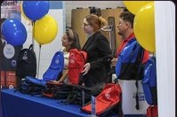 Volunteers in red shirts distributing backpacks under blue and yellow balloons