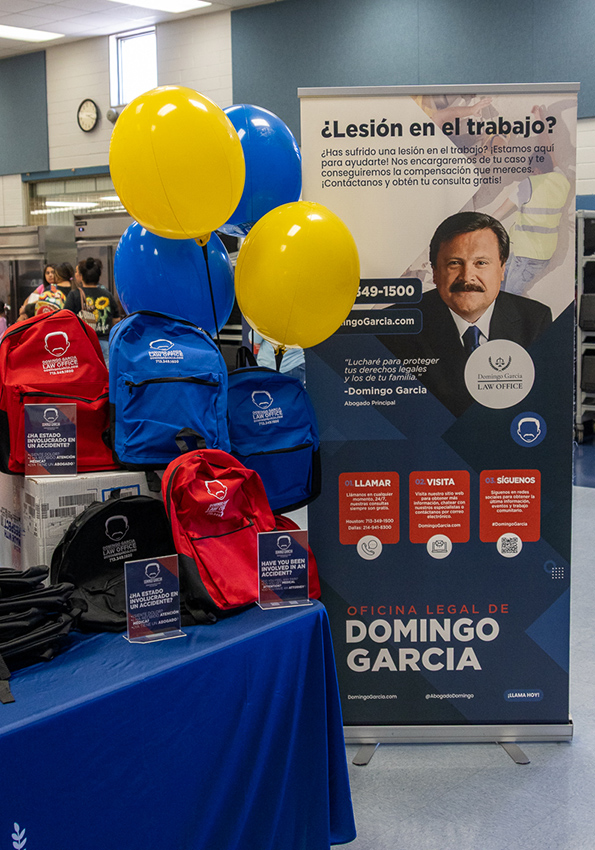 The firm's branded event table at a community expo, with balloons, giveaways and a Spanish-language workplace-injury banner